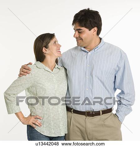 Couple standing smiling at each other against white background View Large Photo Image Stock Photo - Couple standing smiling at each other against white background. Fotosearch