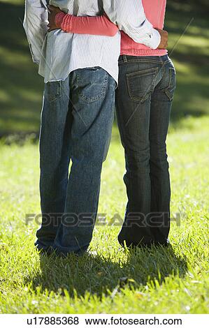 Stock Photo - Low view of couple standing in park with arms around each other. Fotosearch