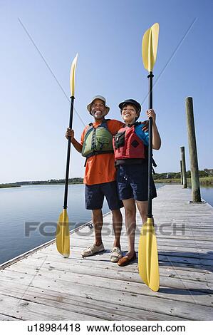 Stock Photo - Middle-aged couple standing on dock holding paddles and smiling at viewer. Fotosearch