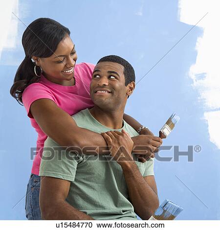 Stock Image - Portrait of male and female couple next to half-painted wall. Fotosearch