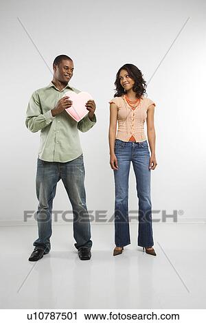 Stock Image - Studio shot of multiethnic couple giving each other valentine heart.. Fotosearch