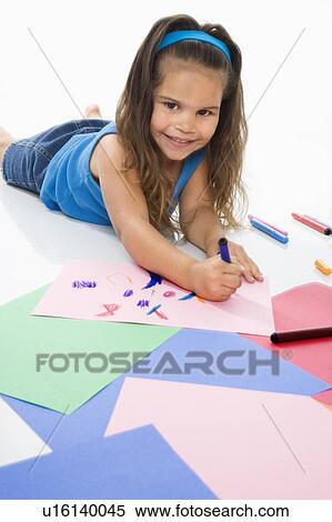 Stock Photography - Young latino girl coloring on construction paper and smiling.. Fotosearch
