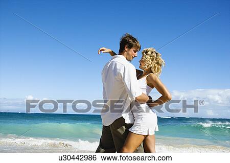Stock Photograph - Attractive couple in embrace on Maui, Hawaii beach.. Fotosearch