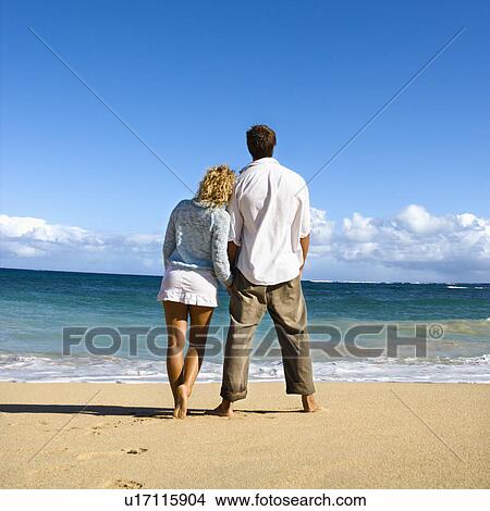 Picture - Attractive couple standing and leaning on each other looking out at ocean in Maui, Hawaii. Fotosearch