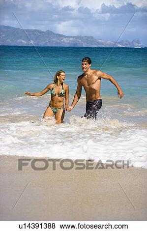 Stock Photo - Couple embracing and smiling as they walk out of water. Fotosearch