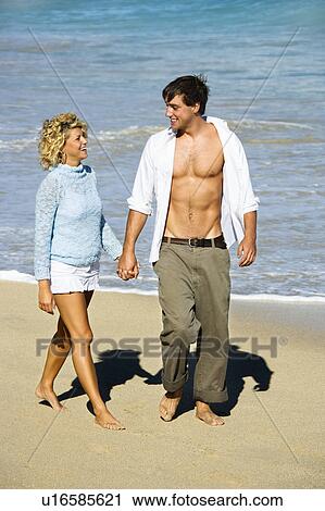 Stock Image - Couple holding hands walking on beach . Fotosearch