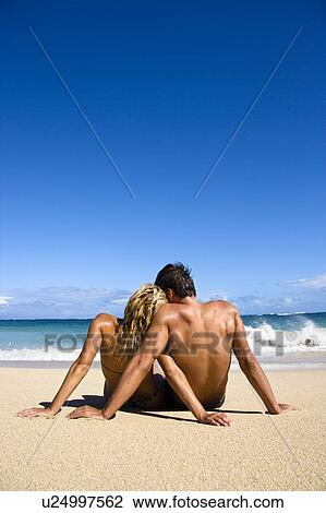 Stock Image - Couple sitting close together on beach. Fotosearch