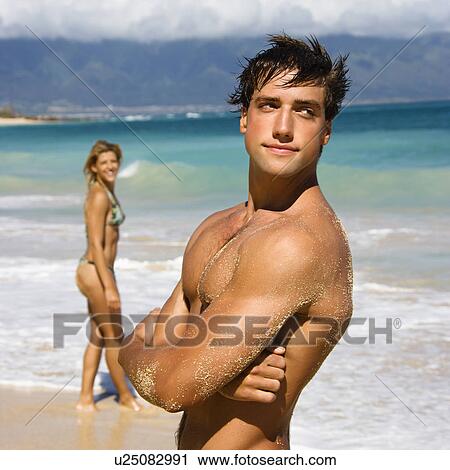 Handsome man standing on Maui, Hawaii beach with woman in background. View Large Photo Image Stock Image - Handsome man standing on Maui, Hawaii beach with woman in background.. Fotosearch