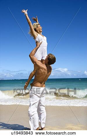 Stock Image - Man holding woman up in air on Maui, Hawaii beach.. Fotosearch