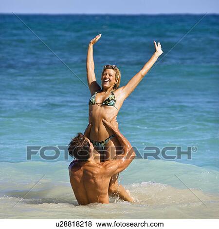 Stock Photo - Man holding woman up out of water on Maui, Hawaii beach.. Fotosearch