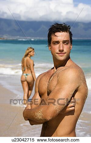 Stock Photography - Man standing on beach with woman in background. Fotosearch