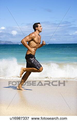 Stock Photo - Physically fit man running on beach. Fotosearch