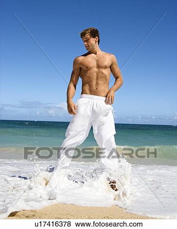 Stock Photo - Physically fit shirtless man standing on Maui, Hawaii beach. Fotosearch