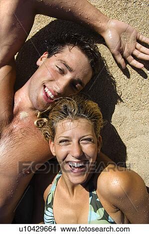 Picture - Smiling happy couple lying in sand on Maui, Hawaii beach.. Fotosearch