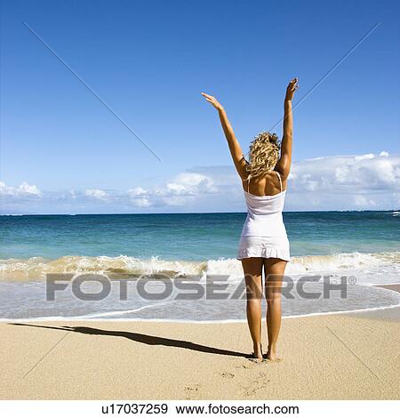 Stock Photo - Woman standing on beach with arms raised. Fotosearch