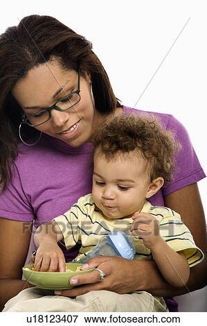 African American mid adult mom sitting with toddler son on lap eating cereal. View Large Photo Image Stock Photo - African American mid adult mom sitting with toddler son on lap eating cereal.. Fotosearch