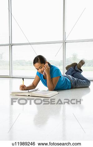 Asian preteen girl lying on floor doing homework while talking on cell phone. View Large Photo Image Stock Photograph - Asian preteen girl lying on floor doing homework while talking on cell phone.. Fotosearch