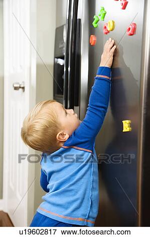 Caucasian toddler boy reaching for magnets on refrigerator. View Large Photo Image Stock Photo - Caucasian toddler boy reaching for magnets on refrigerator.. Fotosearch