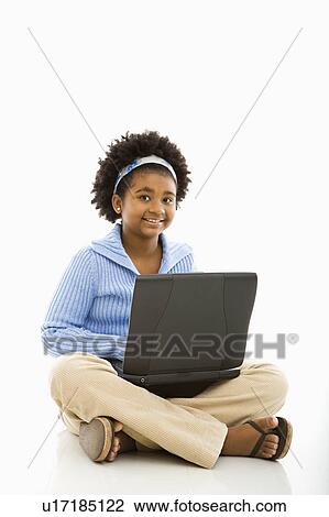 Stock Image - Girl sitting on floor using laptop and smiling at viewer. Fotosearch