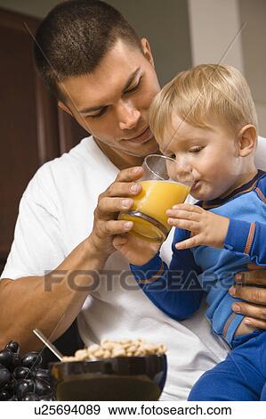 Stock Photo - Man helping toddler son drink juice. Fotosearch