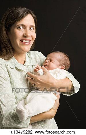 Stock Image - Mother smiling holding baby against black background. Fotosearch