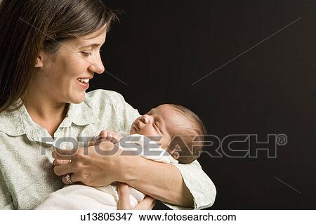 Stock Photo - Mother smiling holding sleeping baby against black background.. Fotosearch