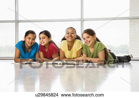 Picture - Preteen girls of mutiple ethnicities sitting together on floor with schoolwork smiling at viewer.. Fotosearch