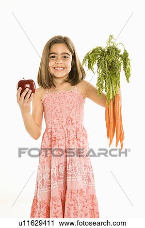 Stock Image - Smiling girl holding bunch of carrots and apple against background.. Fotosearch