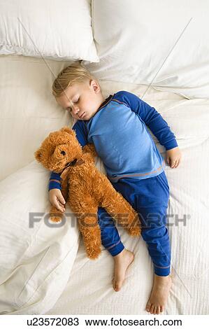 Stock Image - Toddler boy sleeping in bed with teddy bear. Fotosearch