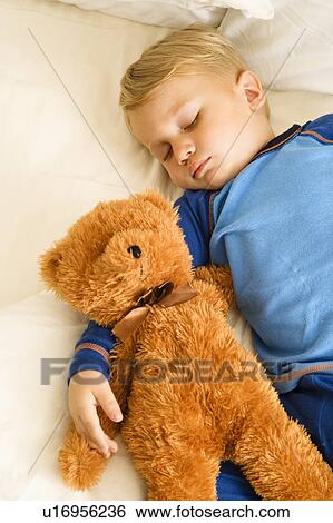 Stock Photograph - Toddler boy sleeping in bed with teddy bear. Fotosearch