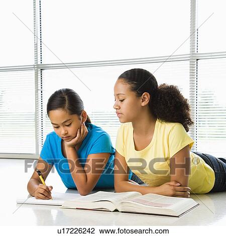 Stock Image - Two preteen girls lying on floor doing homework together.. Fotosearch