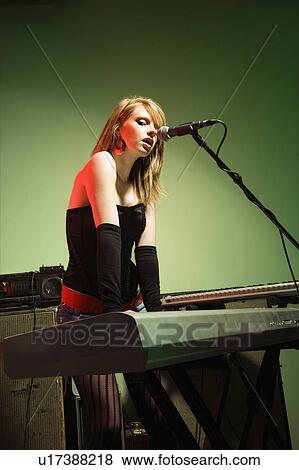 Caucasian female singing into a microphone and playing the keyboard. View Large Photo Image Stock Photo - Caucasian female singing into a microphone and playing the keyboard.. Fotosearch