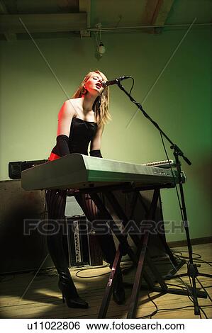 Woman singing into microphone and playing the keyboard View Large Photo Image Stock Photograph - Woman singing into microphone and playing the keyboard. Fotosearch