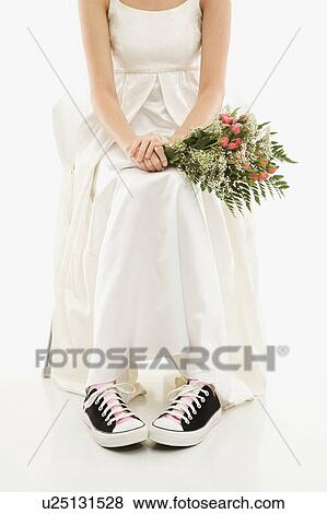 Stock Photo - Caucasian bride holding bouquet exposing her tennis shoes.. Fotosearch