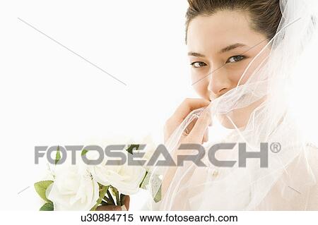 Stock Photography - Portrait of Asian bride with bouquet and pulling veil over face.. Fotosearch