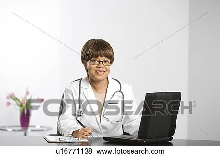 African American middle-aged female doctor sitting at desk working on laptop, smiling and looking at viewer. View Large Photo Image Stock Photo - African American middle-aged female doctor sitting at desk working on laptop, smiling and looking at viewer.. Fotosearch