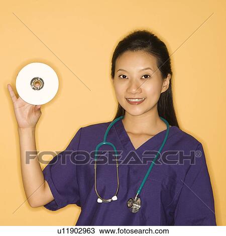 Asian Chinese mid-adult female doctor holding holding up CD against yellow background smiling and looking at viewer. View Large Photo Image Stock Image - Asian Chinese mid-adult female doctor holding holding up CD against yellow background smiling and looking at viewer.. Fotosearch