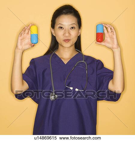 Stock Photography - Asian Chinese mid-adult female doctor holding up giant pills against yellow background smiling and looking at viewer.. Fotosearch