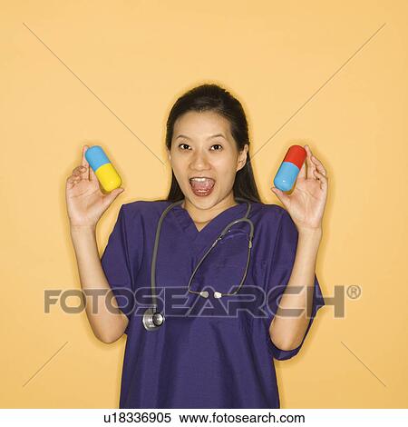 Asian Chinese mid-adult female doctor holding up giant pills against yellow background smiling and looking at viewer. View Large Photo Image Stock Photography - Asian Chinese mid-adult female doctor holding up giant pills against yellow background smiling and looking at viewer.. Fotosearch
