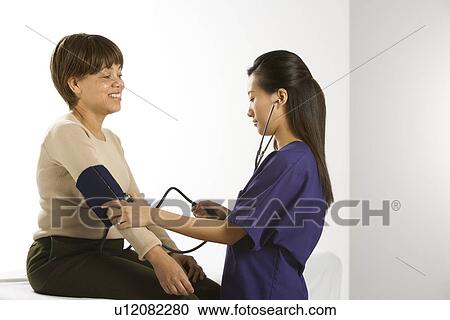 Asian Chinese mid-adult female medical practitioner checking blood pressure of African American middle-aged female patient. View Large Photo Image Stock Image - Asian Chinese mid-adult female medical practitioner checking blood pressure of African American middle-aged female patient.. Fotosearch