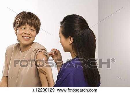 Asian Chinese mid-adult female medical practitioner giving shot in arm of African American middle-aged female patient. View Large Photo Image Stock Photo - Asian Chinese mid-adult female medical practitioner giving shot in arm of African American middle-aged female patient.. Fotosearch
