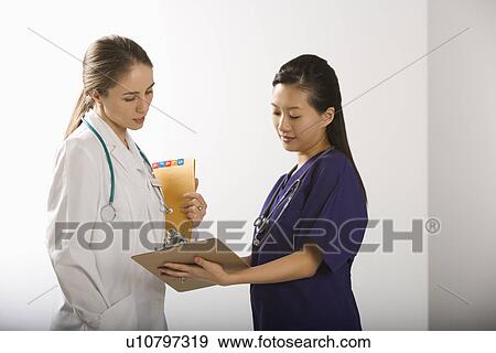 Caucasian mid-adult female doctor and Asian Chinese mid-adult female physician's assistant discussing paperwork. View Large Photo Image Stock Photo - Caucasian mid-adult female doctor and Asian Chinese mid-adult female physician's assistant discussing paperwork.. Fotosearch