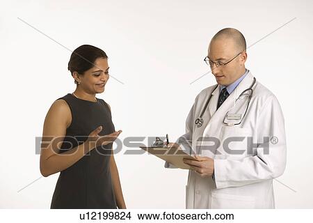 Picture - Caucasian mid adult male physician talking with Indian woman patient.. Fotosearch