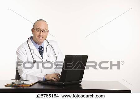 Caucasian mid adult male physician sitting at desk with laptop computer. View Large Photo Image Picture - Caucasian mid adult male physician sitting at desk with laptop computer.. Fotosearch