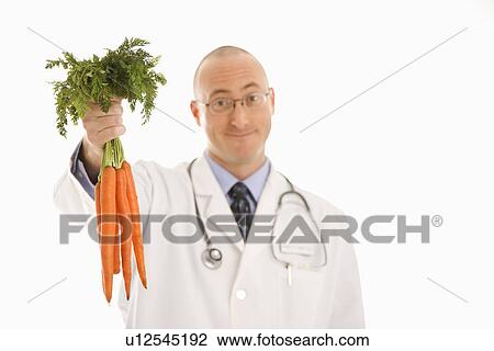 Stock Image - Caucasian mid adult male physician holding bunch of carrots.. Fotosearch