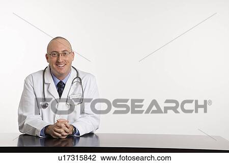 Caucasian mid adult male physician sitting at desk smiling. View Large Photo Image Stock Image - Caucasian mid adult male physician sitting at desk smiling.. Fotosearch