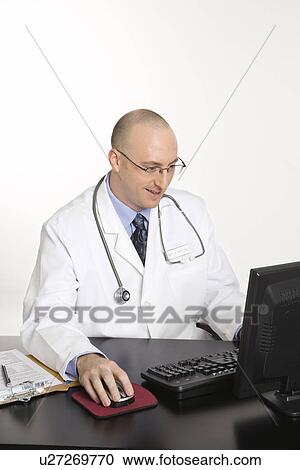 Stock Image - Caucasian mid adult male physician sitting at desk with laptop computer.. Fotosearch