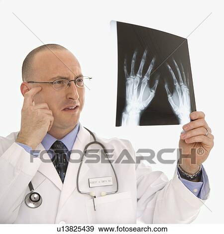 Caucasian mid adult male physician holding up hand xrays looking perplexed. View Large Photo Image Stock Photo - Caucasian mid adult male physician holding up hand xrays looking perplexed.. Fotosearch