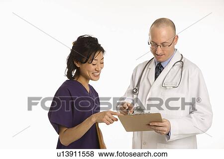 Stock Photo - Caucasian mid adult male physician talking with Asian woman doctor.. Fotosearch