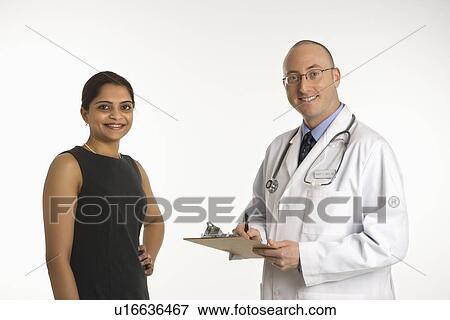 Stock Photo - Caucasian mid adult male physician talking with Indian woman patient.. Fotosearch